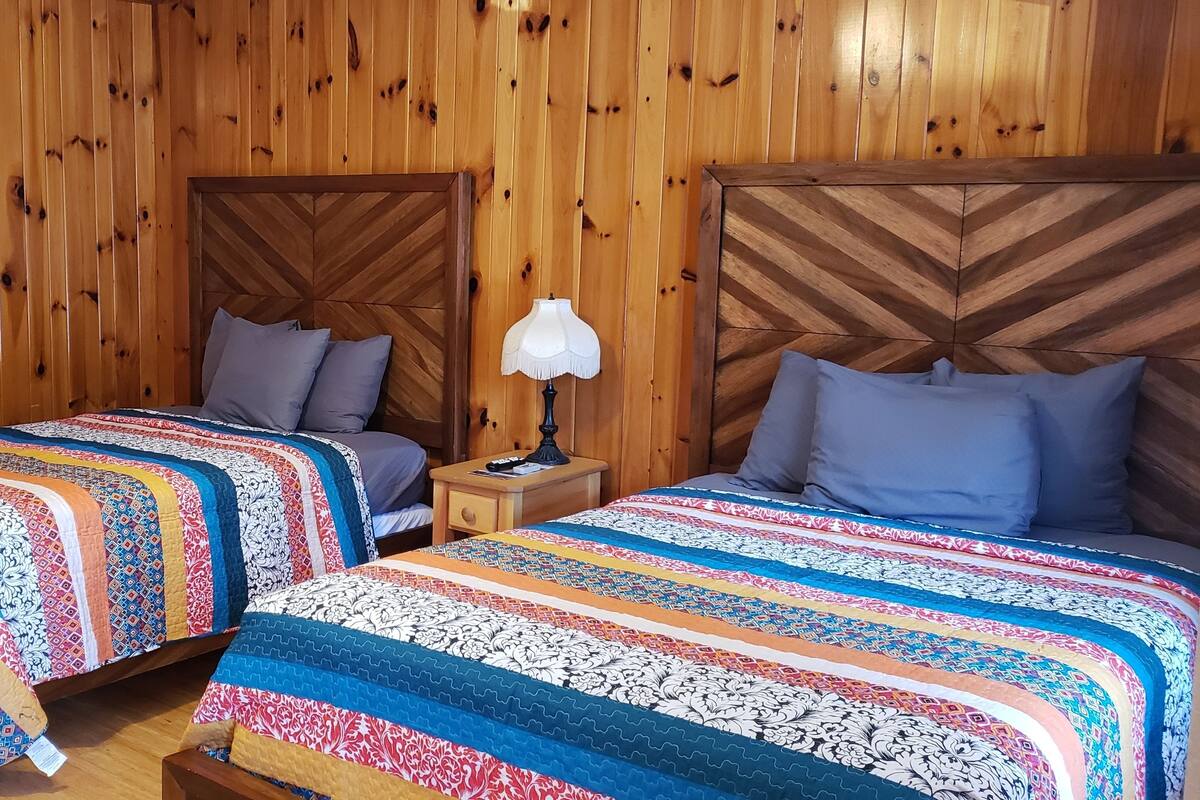 Ein Zimmer mit zwei Holzbettgestellen, jeweils mit einem Kopfteil und einem Nachttisch mit Lampe.