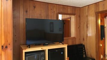A wooden-paneled room with a flat-screen TV on a wooden stand, a microwave, and a refrigerator.