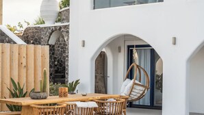 Un espacio exterior moderno para comer, con una mesa y sillas de madera, un sillón colgante y un jacuzzi.