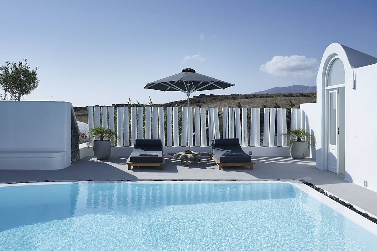 A swimming pool with lounge chairs and an umbrella, surrounded by white walls and a fence.