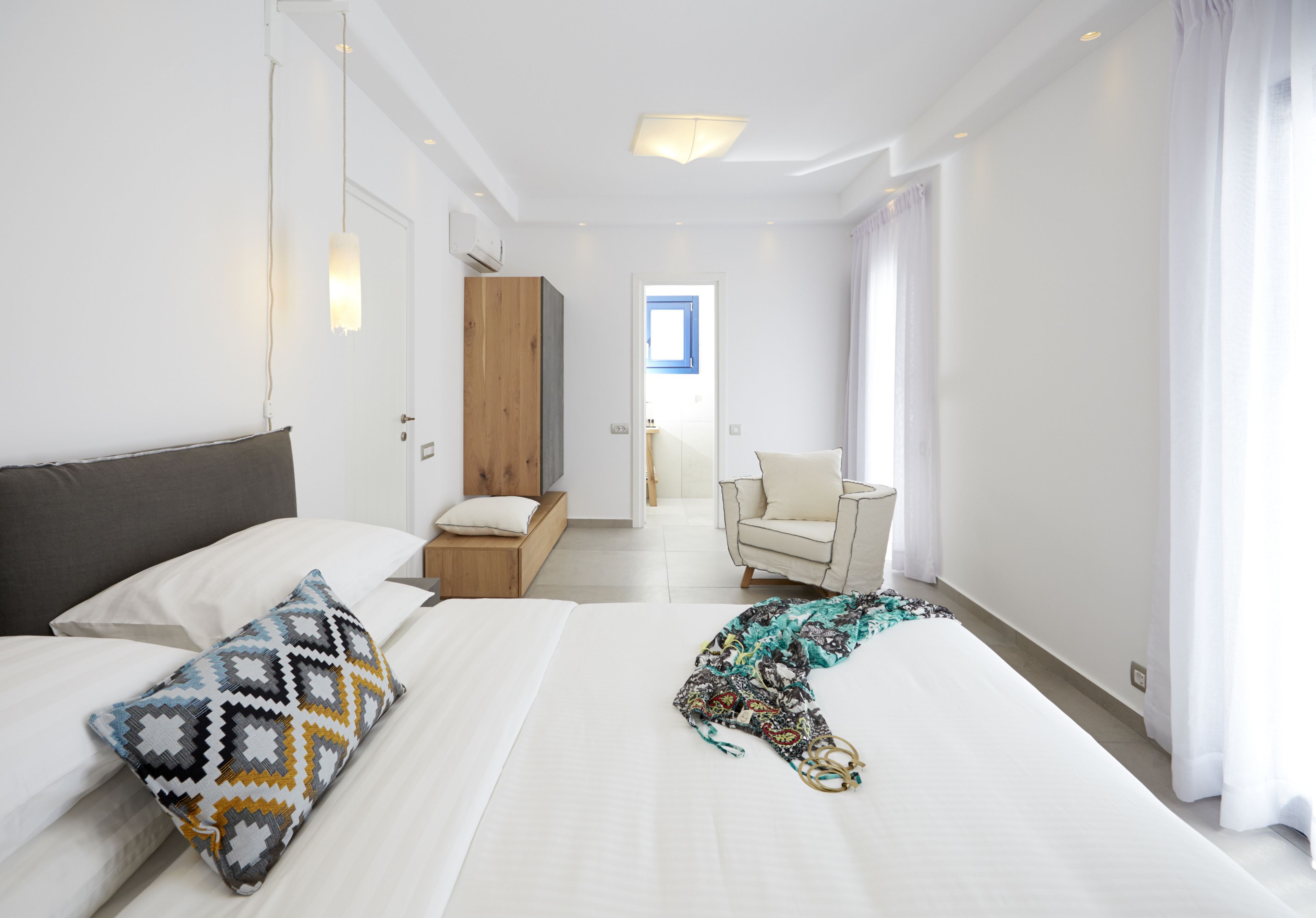 Una camera d'albergo moderna con un letto grande, un armadio in legno, una sedia e vista sull'esterno attraverso una finestra.