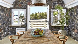Comedor con pared de piedra, una mesa de madera, sillas de mimbre y una lámpara colgante.