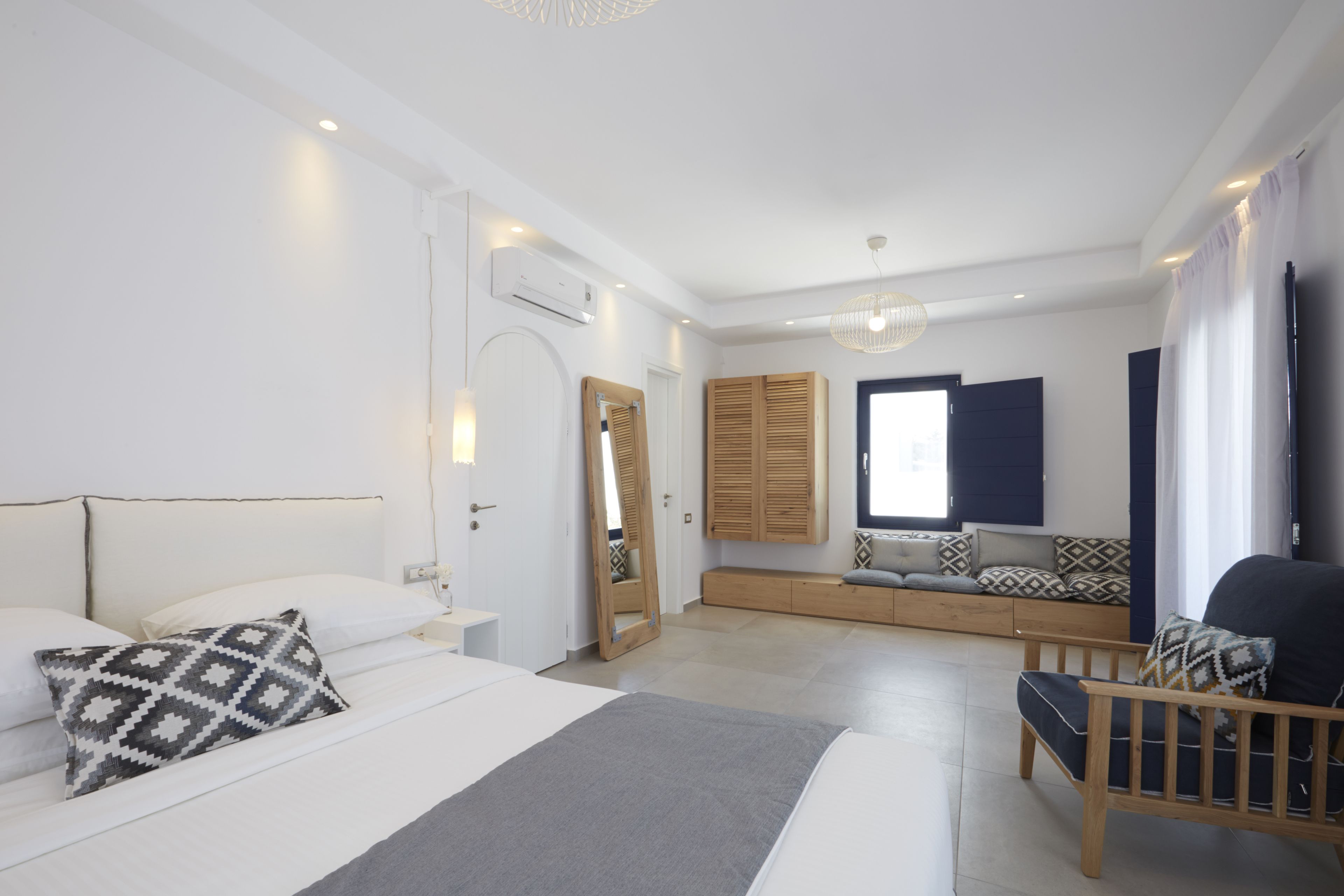 Un dormitorio moderno con una cama grande, un banco de madera, una silla y un televisor.