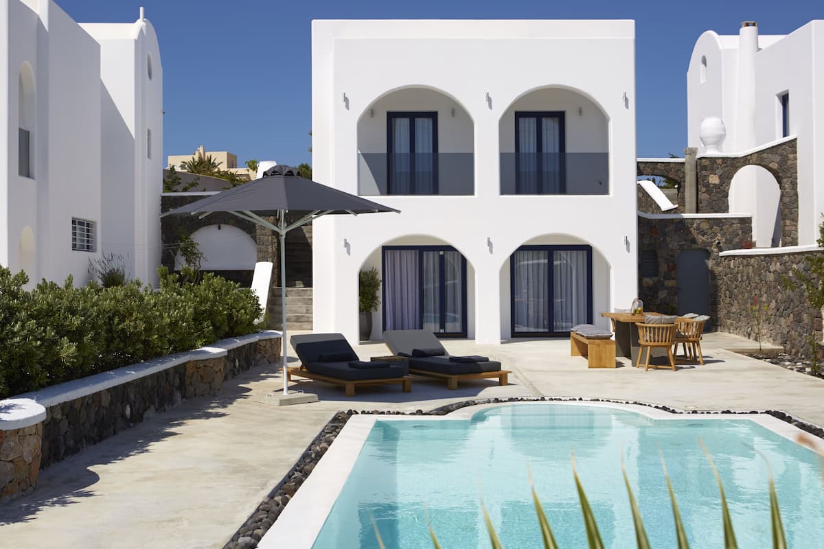 A modern white villa with a swimming pool, sun loungers, and a stone wall.