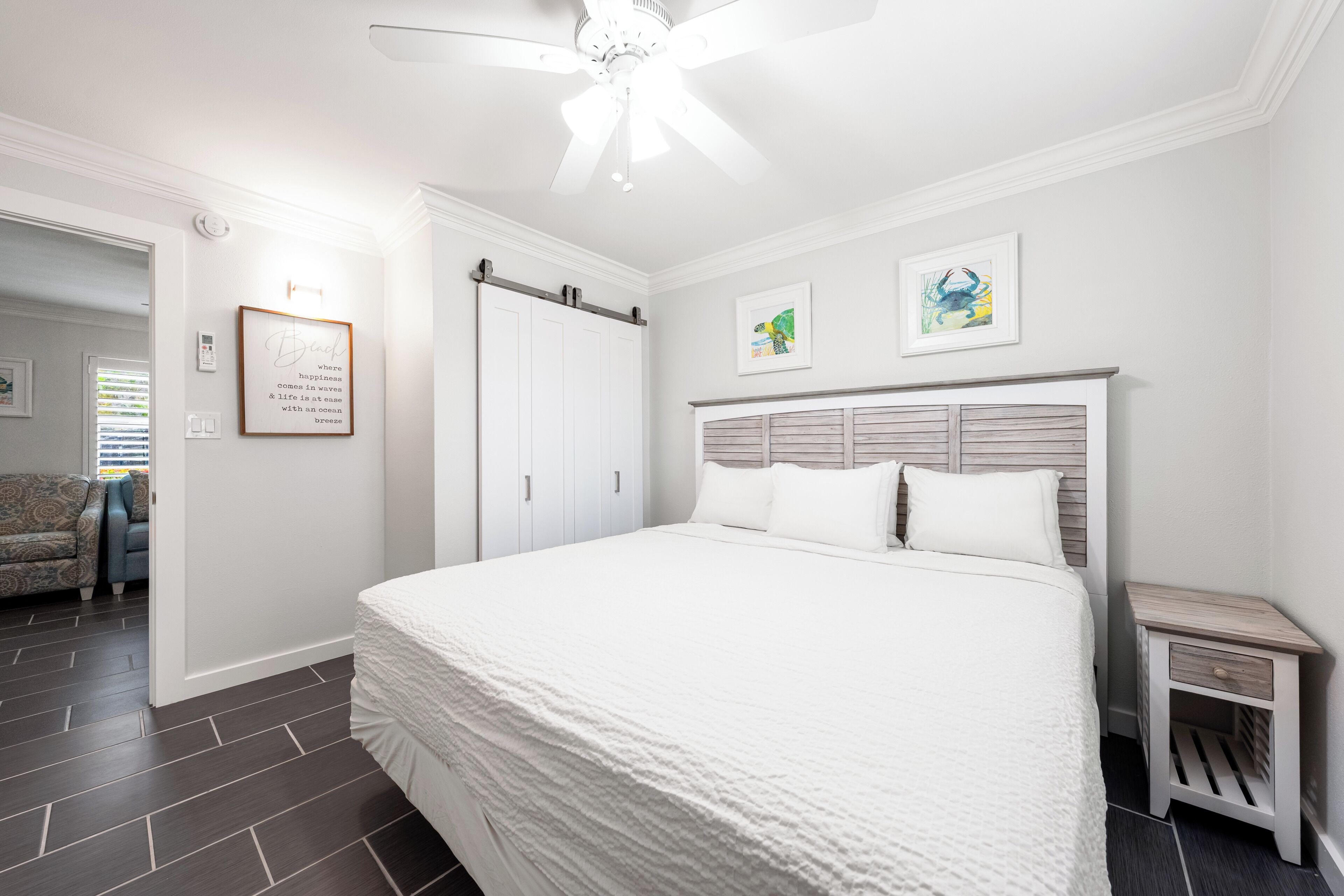 A bedroom with a large bed, a ceiling fan, a wardrobe, and two framed pictures on the wall.