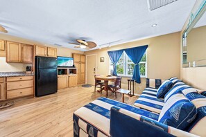 A compact kitchen with wooden cabinets and a black refrigerator, a dining area with a table and chairs, and a sofa with striped cushions.