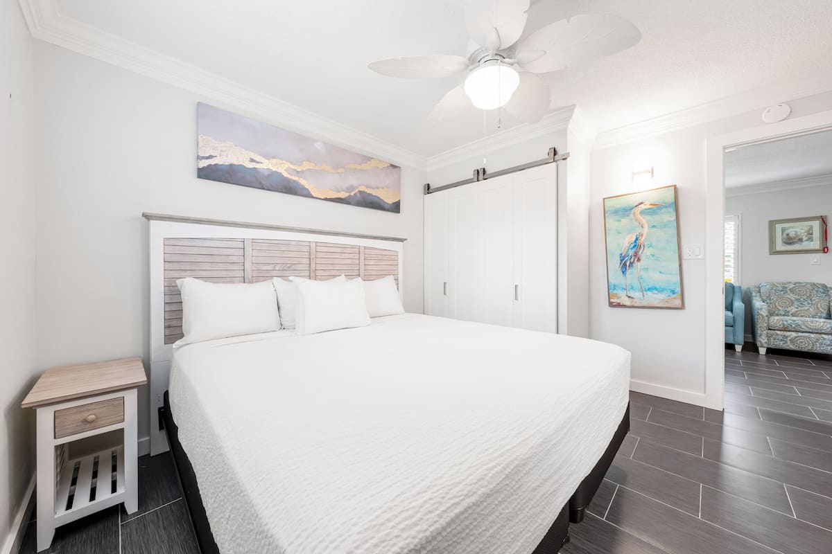 A bedroom with a large bed, a nightstand, a ceiling fan, and artwork on the walls.