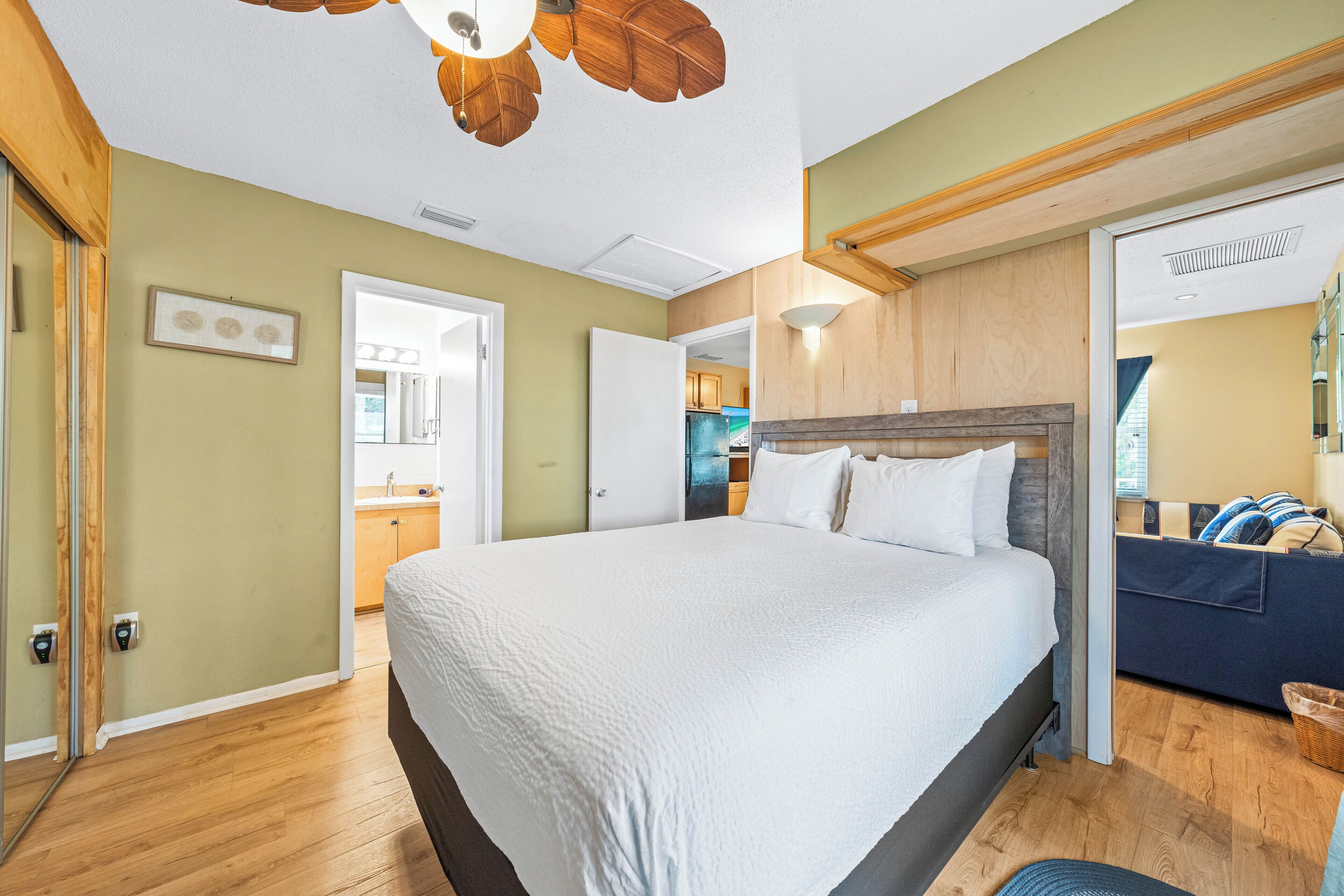 A bedroom with a large bed, wooden ceiling, and a view into the kitchen.
