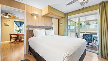 Ein Hotelzimmer mit einem großen Bett, einem Schreibtisch mit Stuhl, einem Deckenventilator und Blick ins Freie durch eine Schiebetür.