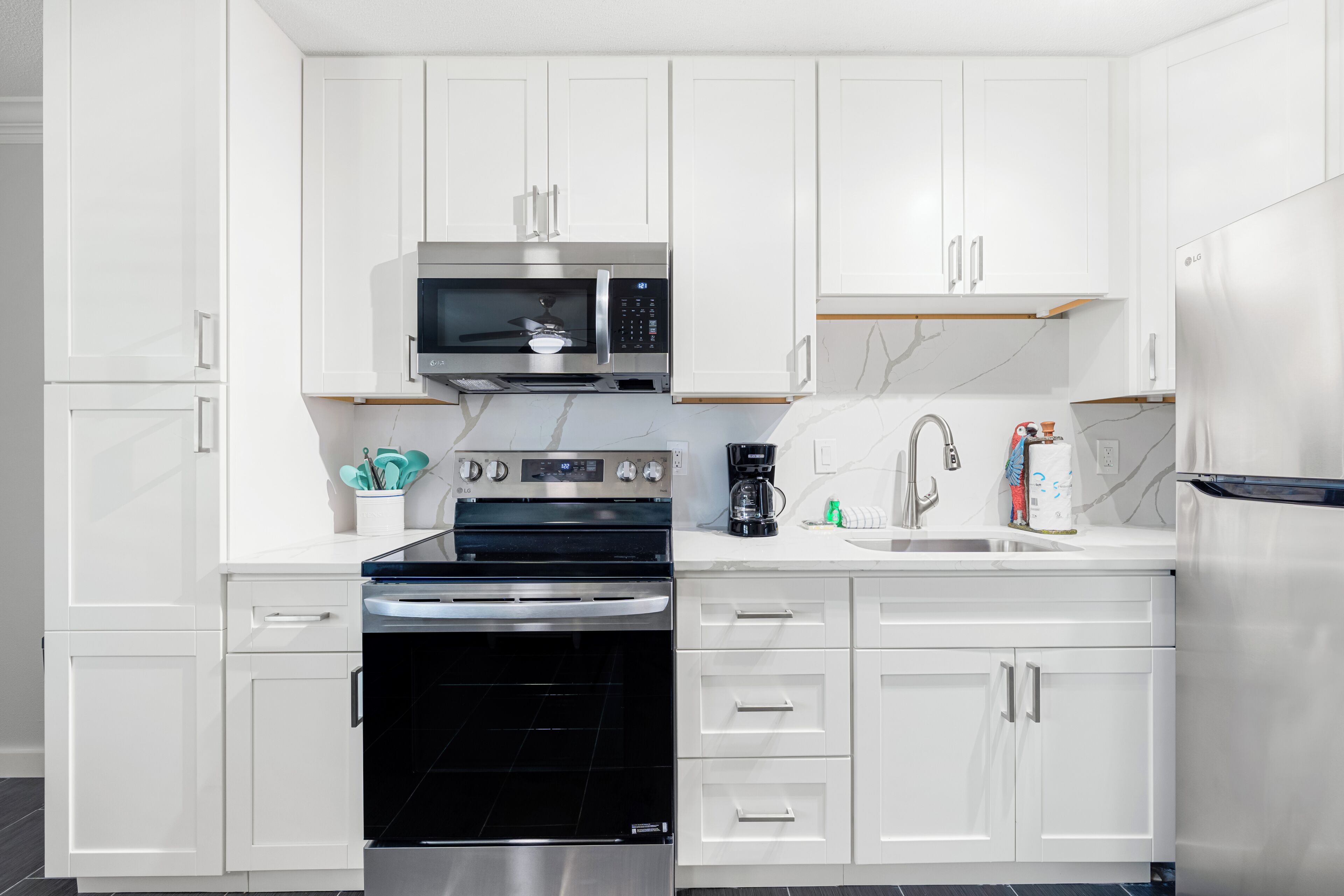 A modern kitchen with white cabinetry, a built-in microwave, a stove, and a coffee maker.