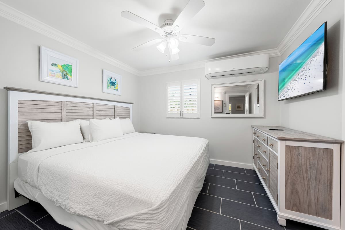 A bedroom with a bed, a ceiling fan, a TV, and a dresser.