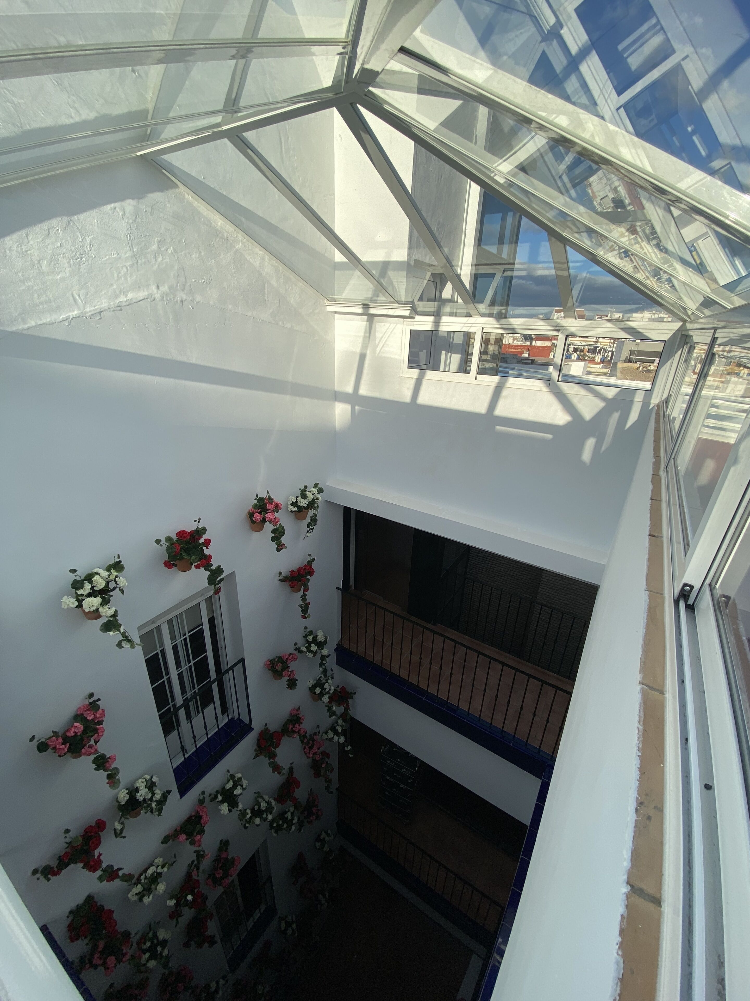 Un interior de varios niveles con techo de vidrio, balcones y plantas en macetas.
