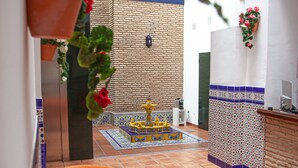 A courtyard with a tiled floor, a yellow table with a blue and yellow pattern, and a brick wall.