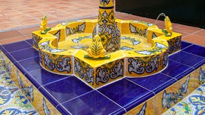 A fountain with intricate tile work and hanging flower baskets in a lobby area.