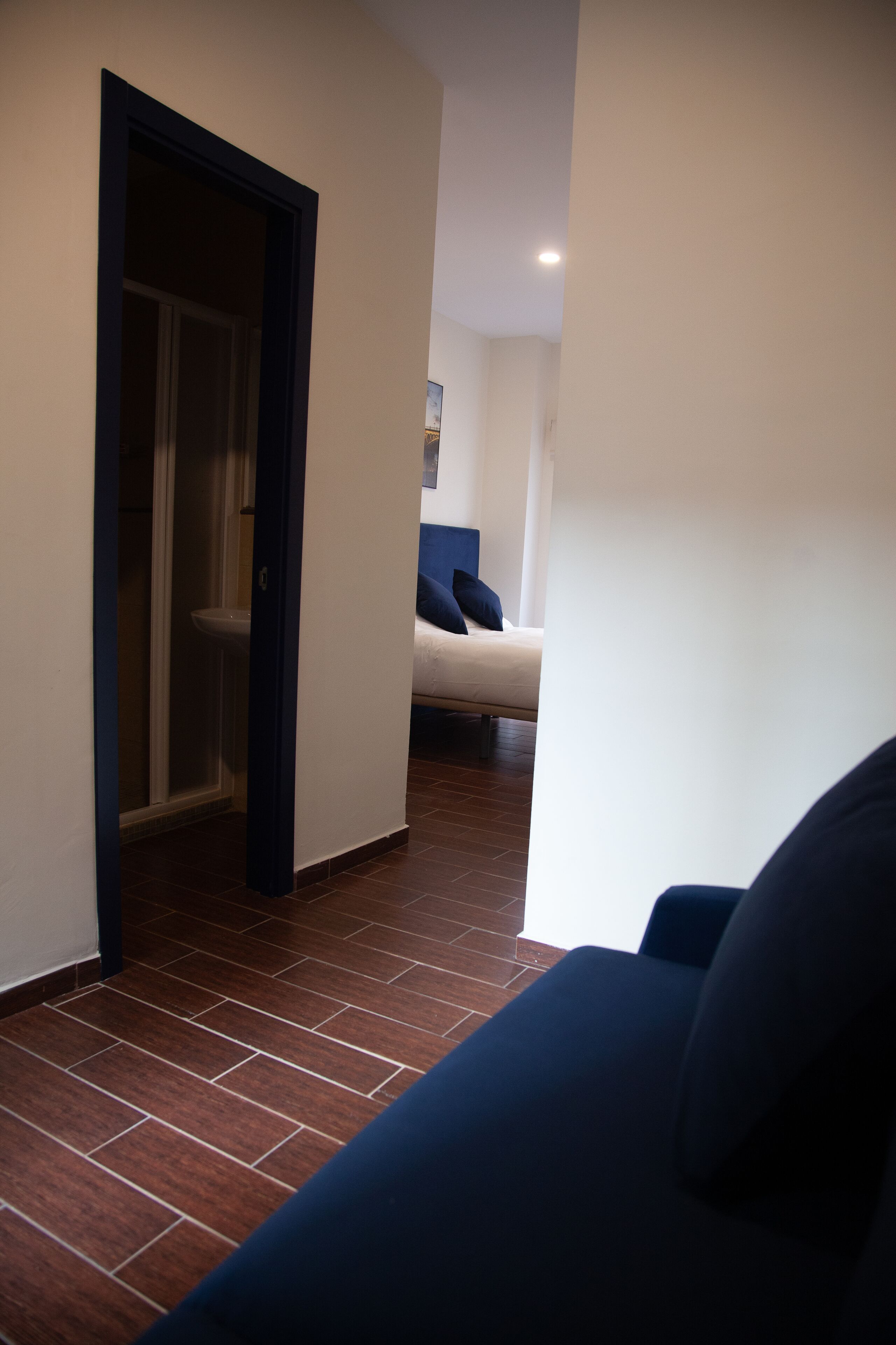 A hallway with a dark blue couch, a white wall, and a door leading to a bathroom.