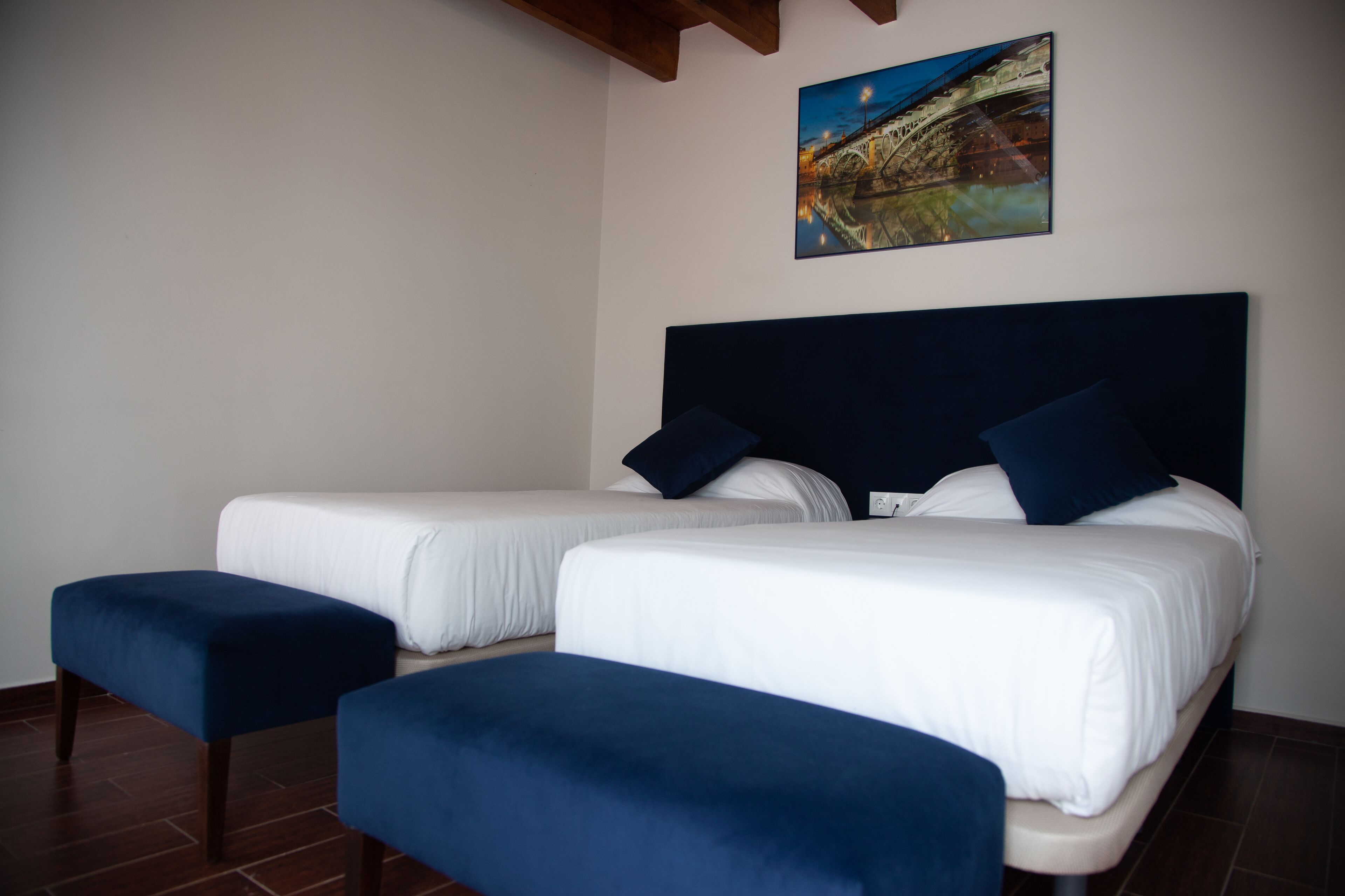 Habitación de hotel con dos camas, cabecera oscura y un cuadro de un puente en la pared.