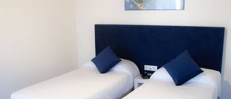 Habitación de hotel con dos camas individuales, cada una con cabecera azul y cojines a juego, techo de madera y un cuadro de un puente en la pared.