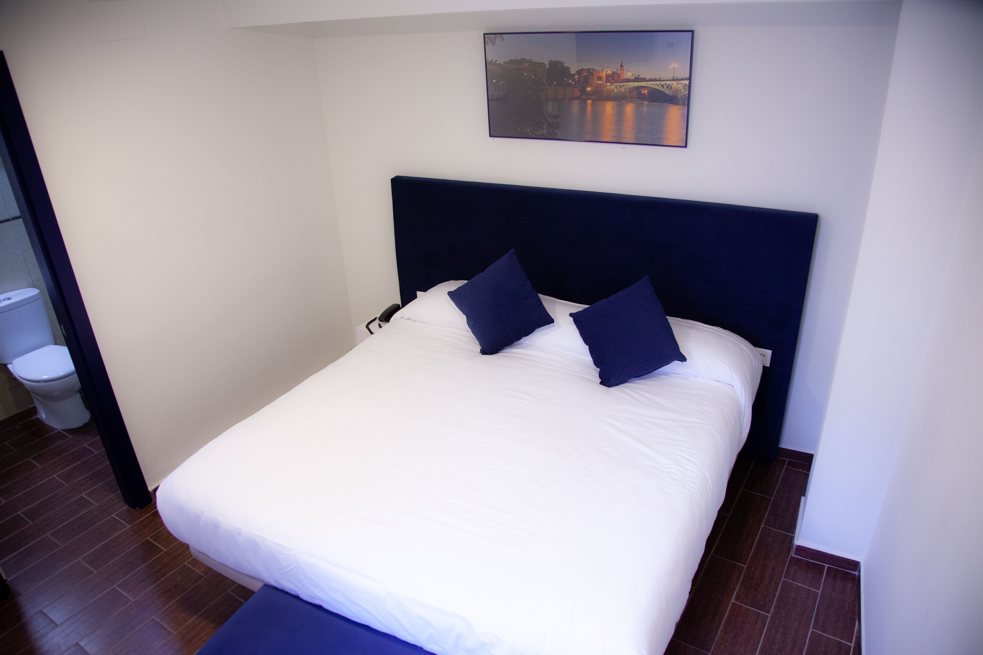 A neatly made bed with a dark headboard, white bedding, and two dark pillows.