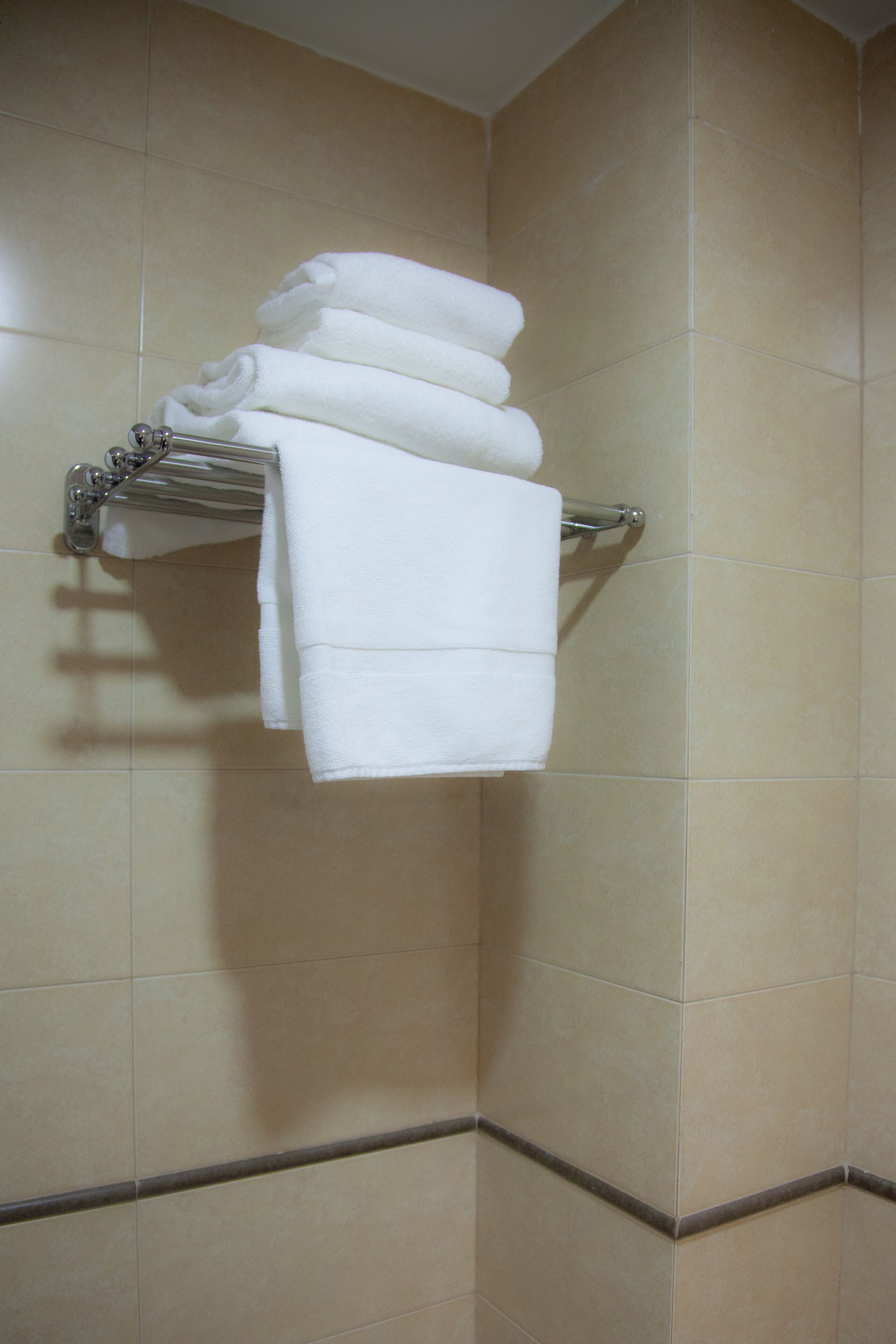 Esquina de un baño con paredes de azulejos color beige y un perchero con toallas blancas dobladas.
