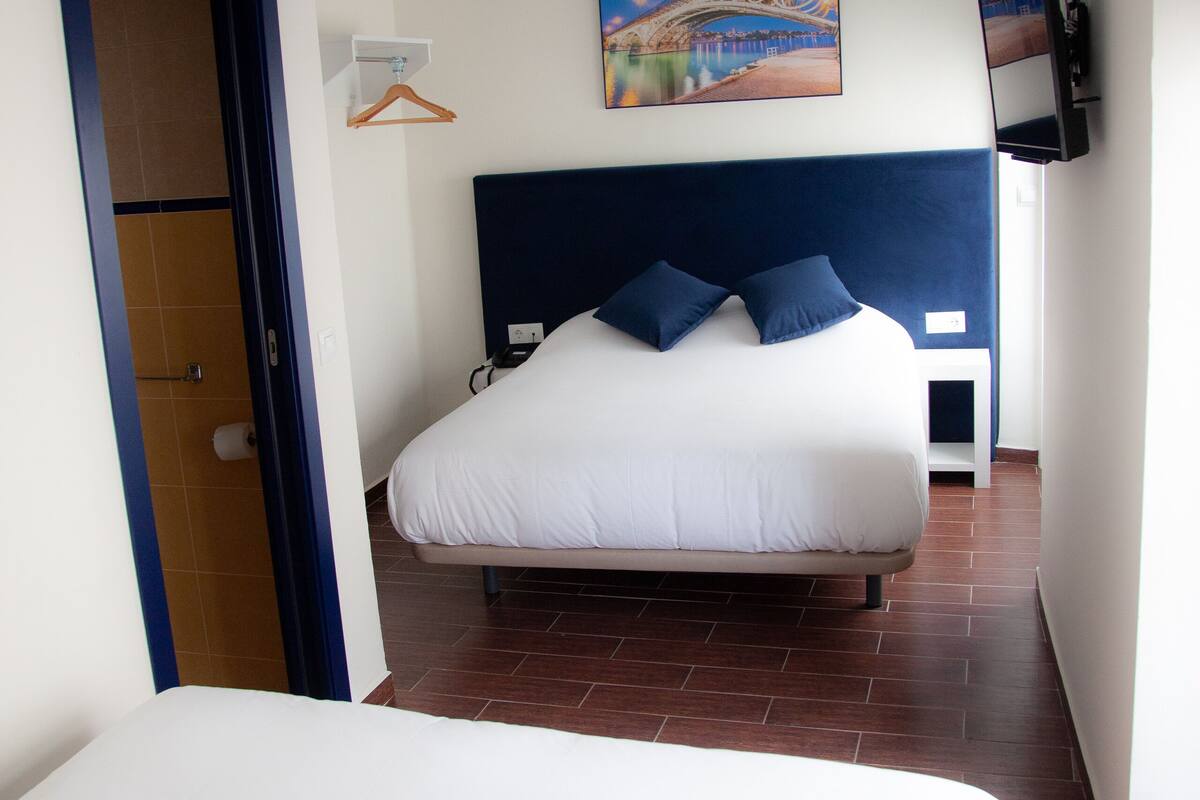 A hotel room with a large bed, a headboard, a painting on the wall, and a television mounted on the wall.