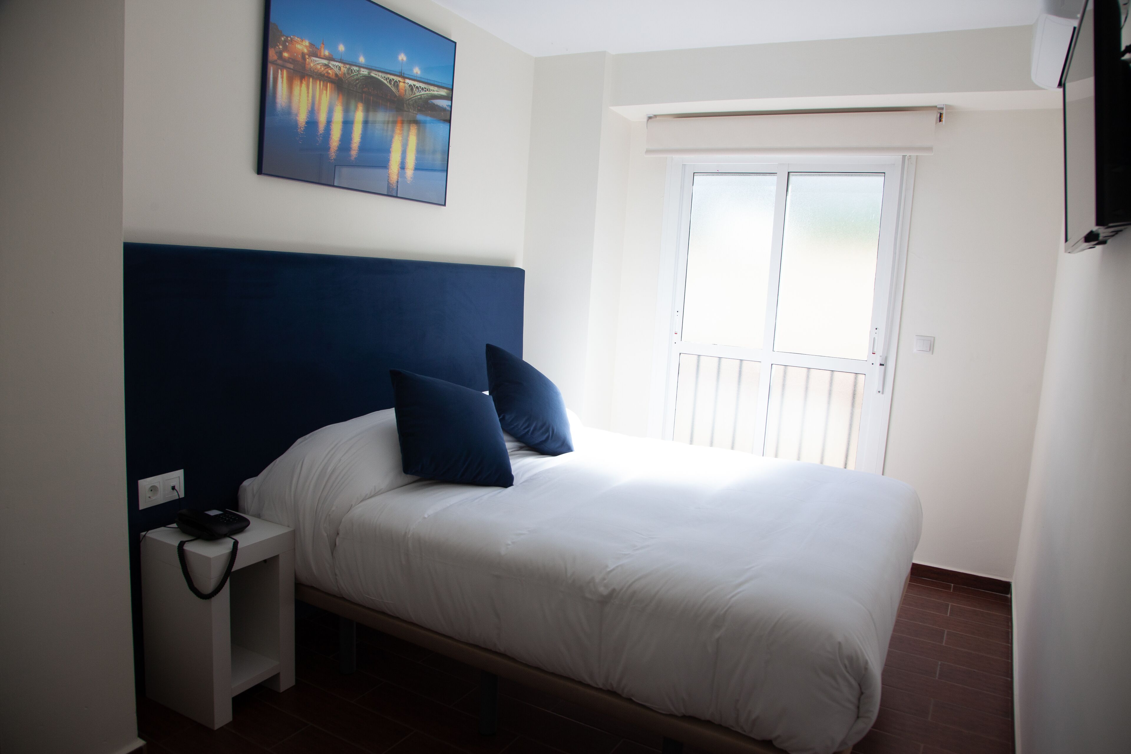 A bedroom with a bed, a nightstand, a painting, and a window.