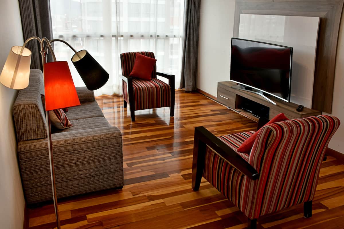 A modern living room with a sofa, striped armchairs, a TV, and a lamp.