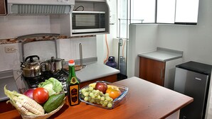 A kitchen with a stove, microwave, and refrigerator. There is a basket of vegetables and a bowl of fruit on the counter. - Polo Apartment (Cusco)