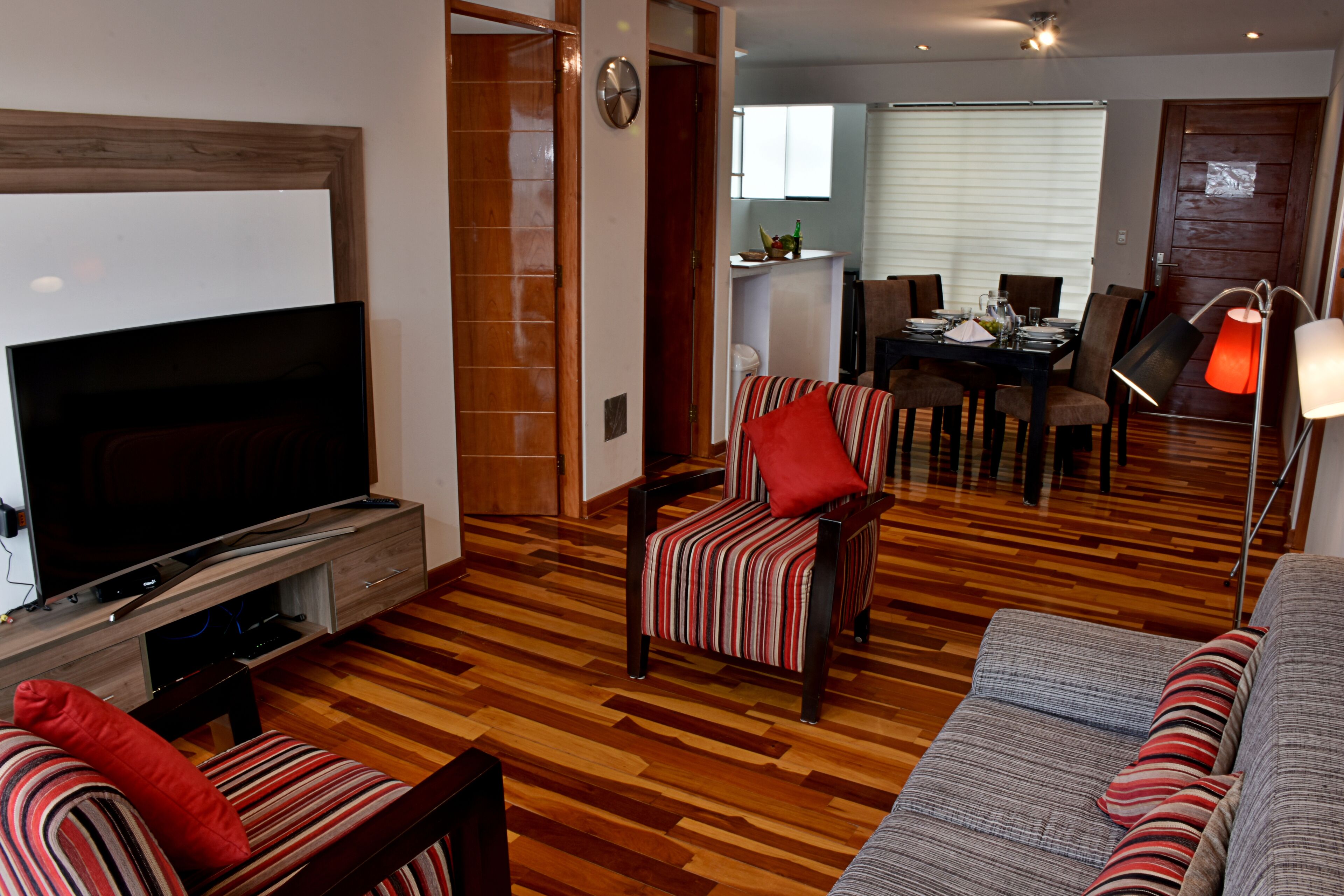 A living room with a flat-screen TV, striped armchairs, a sofa, and a dining area with a table and chairs.