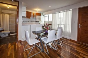 Une cuisine moderne avec des meubles blancs, une table à manger entourée de chaises blanches et une grande fenêtre agrémentée de rideaux.