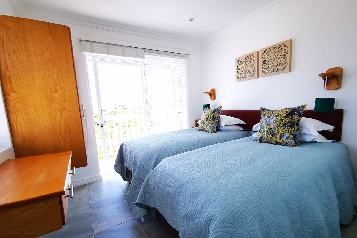 Ein Schlafzimmer mit zwei Betten, einem Holztisch und einer Schiebetür zu einem Balkon.