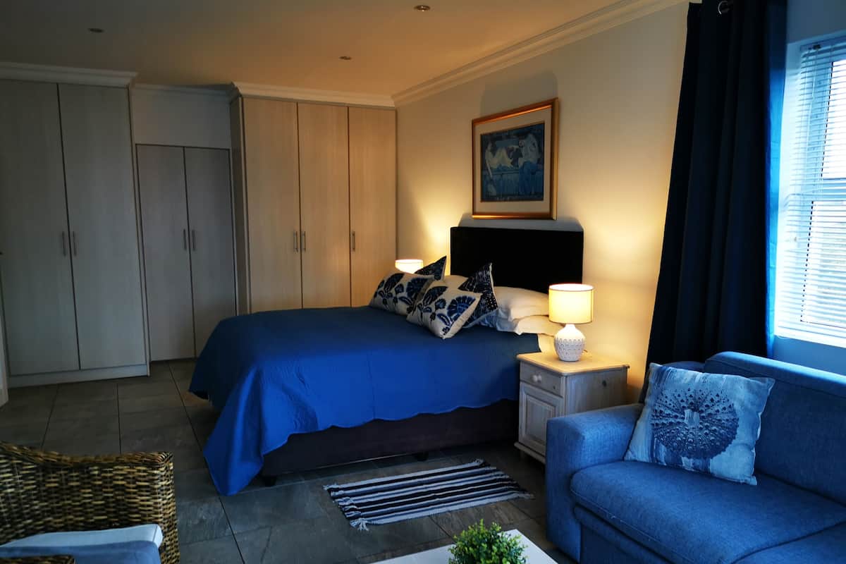 Ein Schlafzimmer mit Bett, Nachttischen, einer Lampe, einem Sofa, einer Topfpflanze, einem Bild und einem Kleiderschrank.