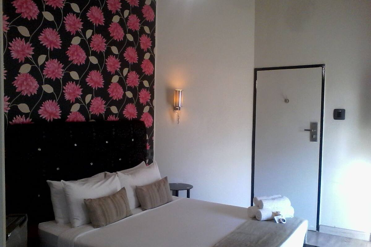 Une chambre d’hôtel avec un lit, une table de chevet, une lampe fixée au mur et une porte.