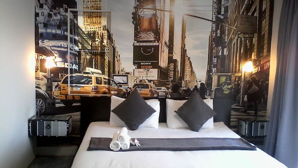 Een hotelkamer met een bed, kussens, een deken en een muurschildering van een stadsgezicht.