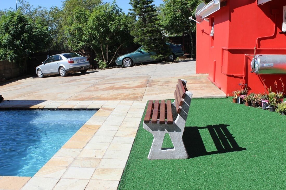 A swimming pool with a bench, a red building, and parked cars.