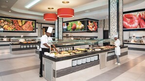 Un espace buffet proposant différents stands de nourriture, des chefs qui servent les plats et de grands écrans présentant les plats.
