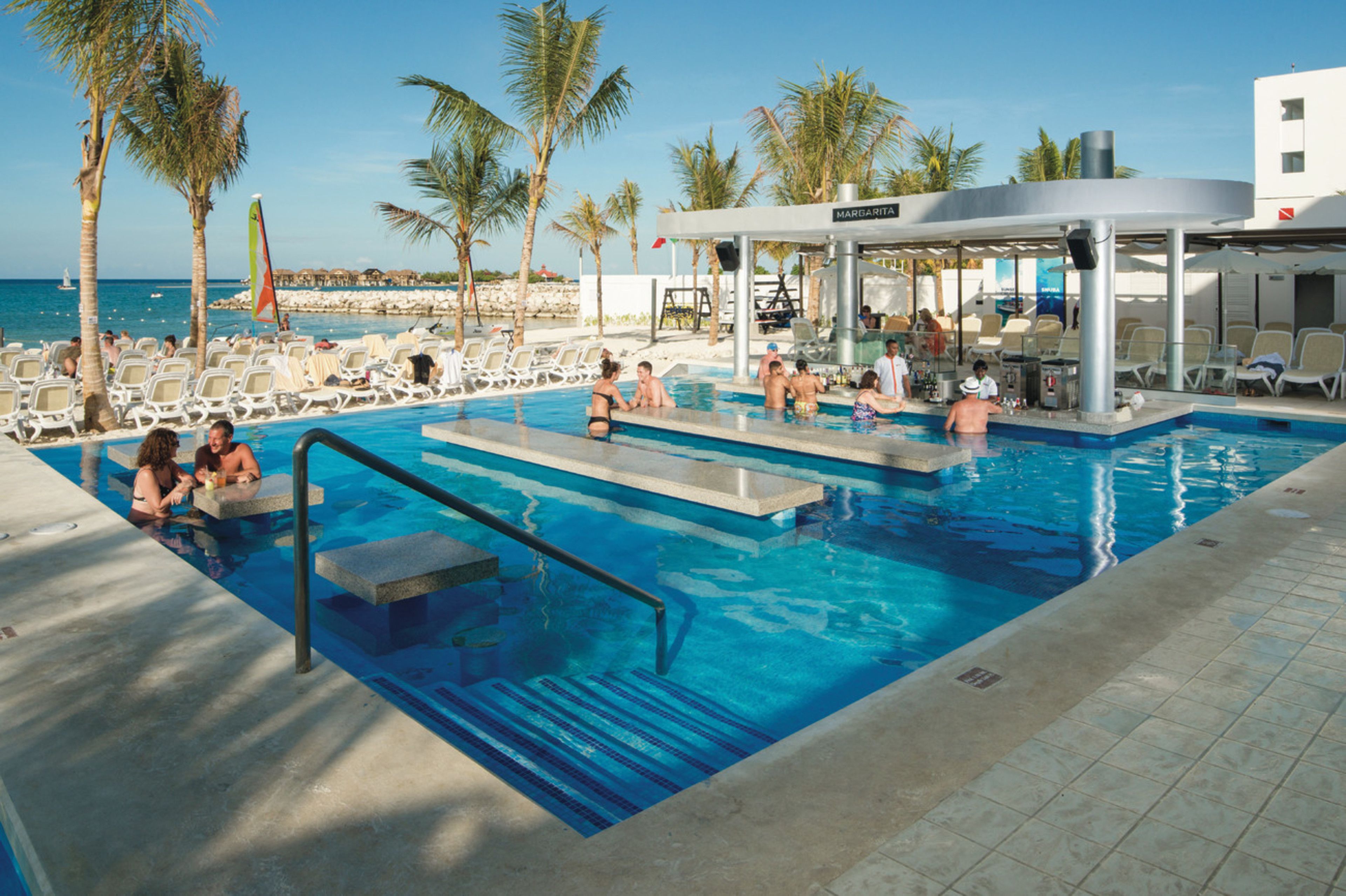 A pool area with lounge chairs, a covered seating area, and a view of the ocean.
