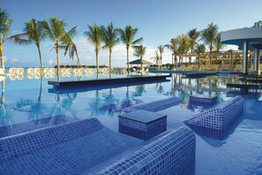 A pool with tiled lounge areas, palm trees, and a clear sky. - Hotel Riu Reggae - Adults Only - All Inclusive (Montego Bay)