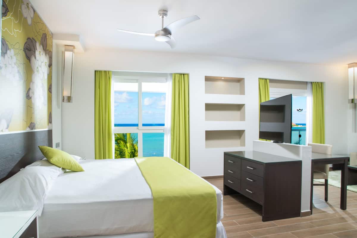 A hotel room with a bed, a desk, a chair, a TV, and a view of the ocean.