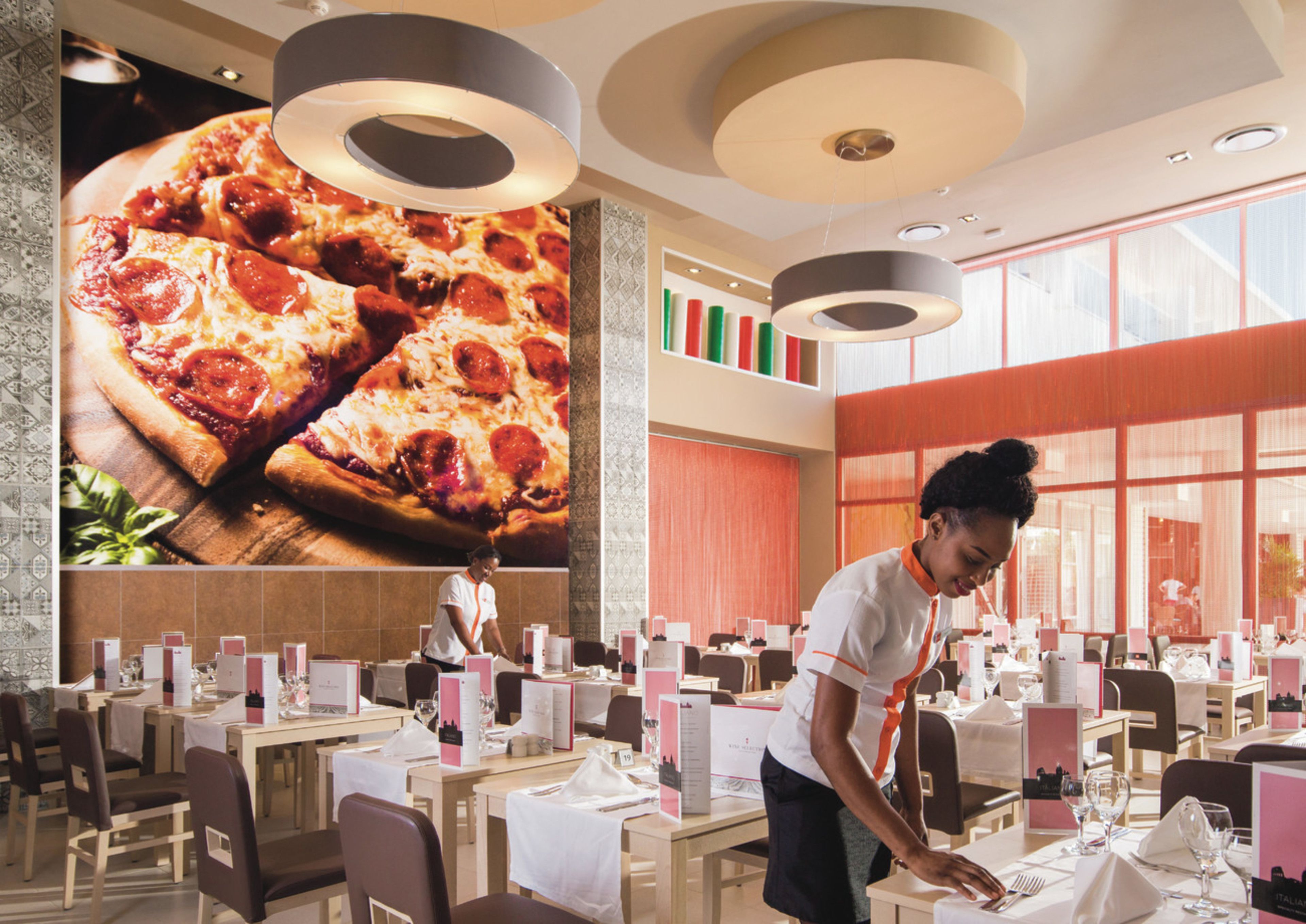 A restaurant with a large pizza mural on the wall, multiple dining tables with white tablecloths, and a modern ceiling design.