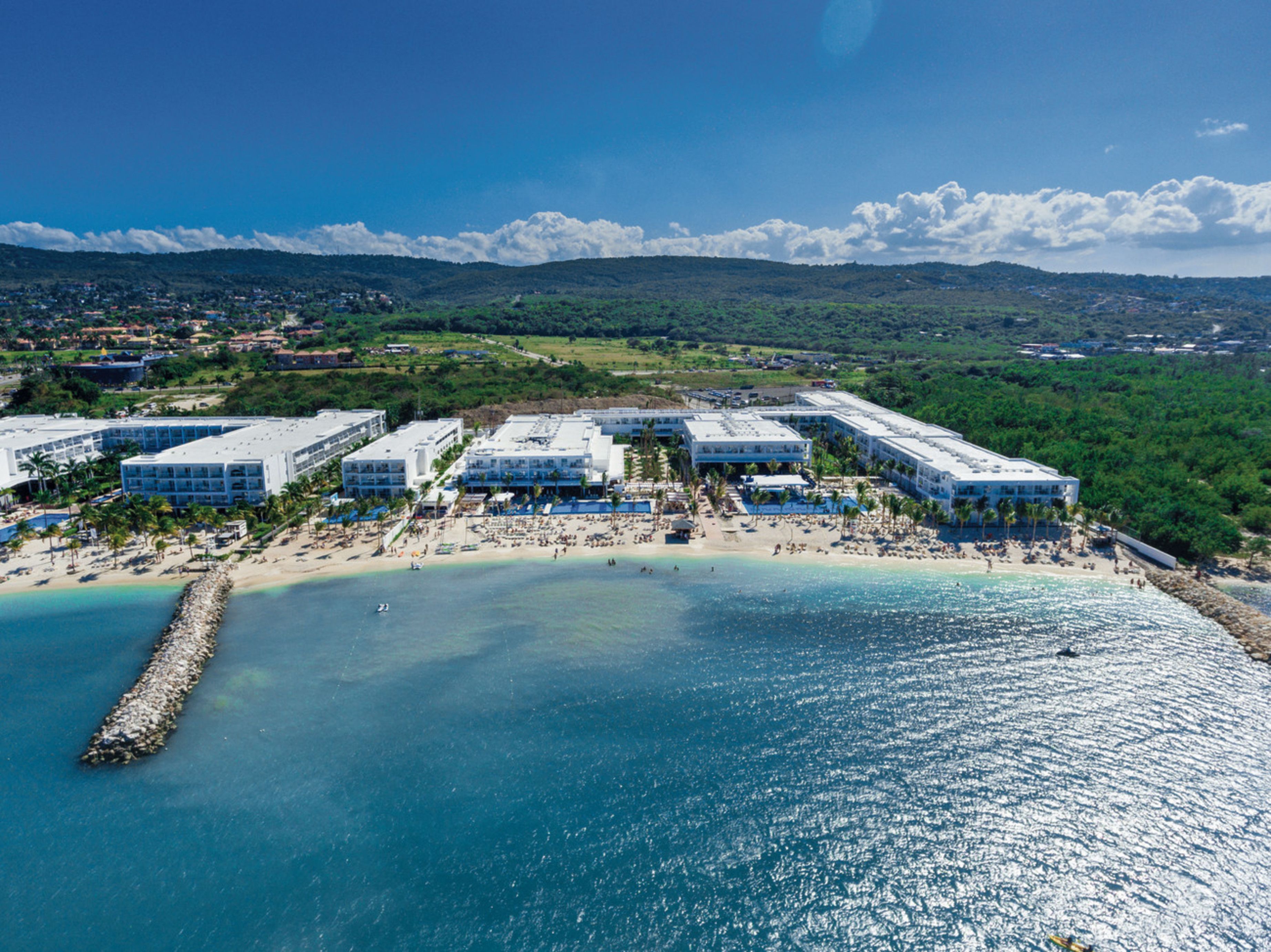 An aerial view of a coastal hotel with multiple buildings, a beach, and a clear blue sky.