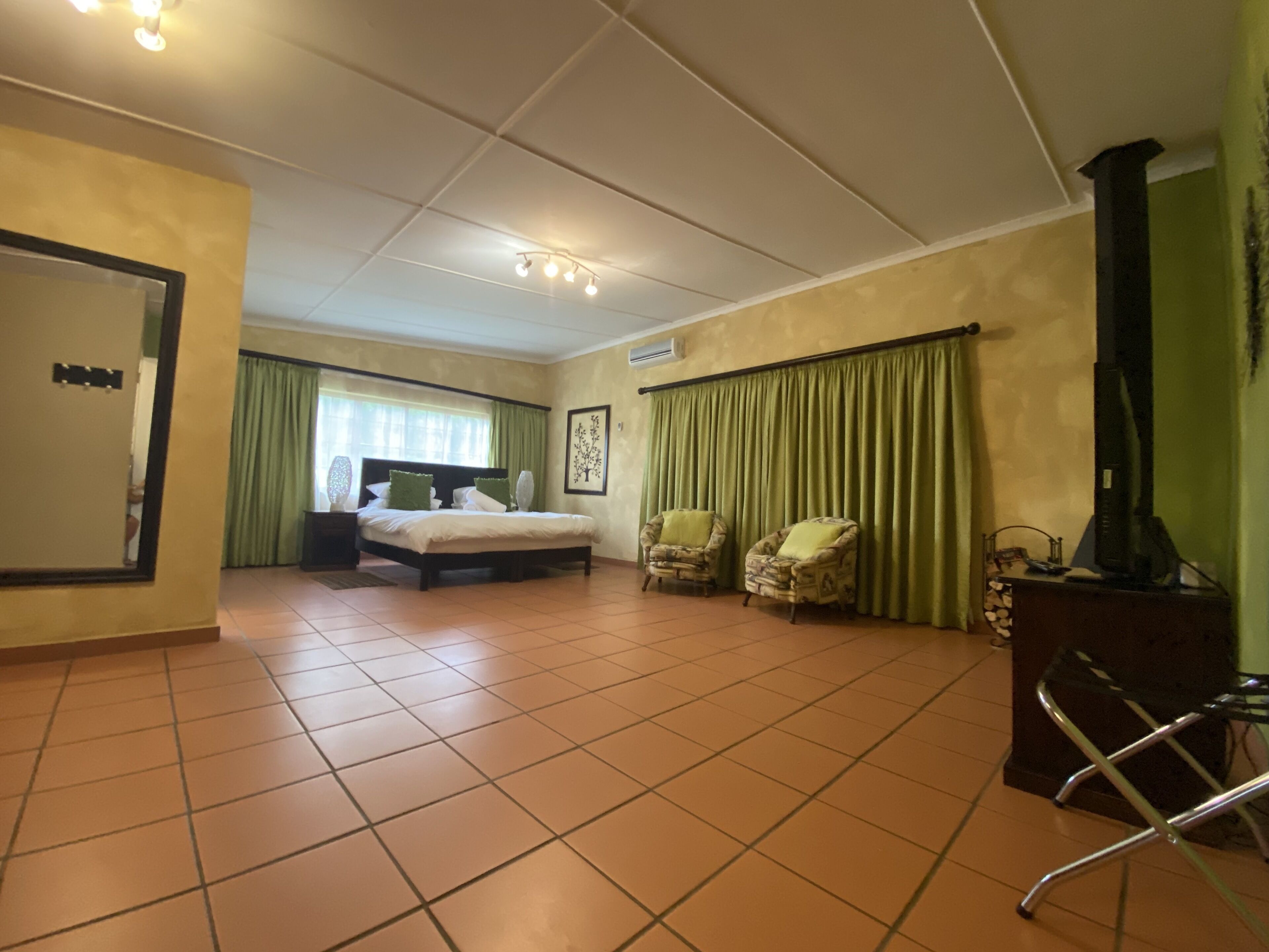 A hotel room with a bed, two armchairs, a desk with a computer, and a television.