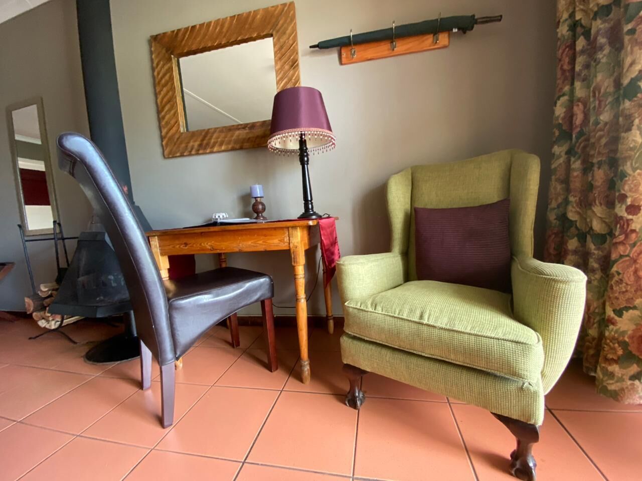 A room with a wooden desk, a green armchair, a purple lamp, and a mirror on the wall.