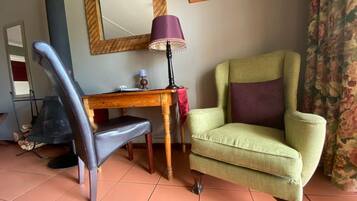 A room with a wooden desk, a green armchair, a purple lamp, and a mirror on the wall.