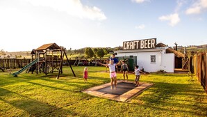 A playground with a slide and swings, a small building labeled "CRAFT BEER", and a grassy area. - St Ives Lodge (Lidgetton West)