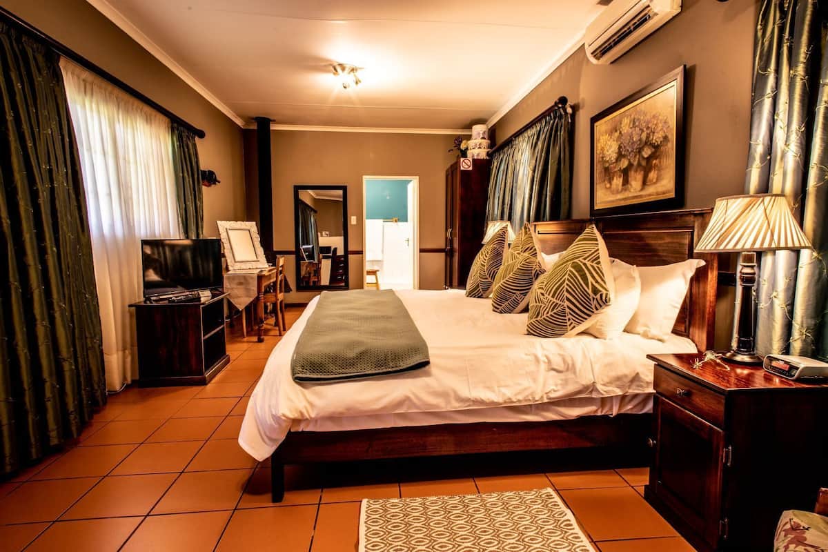 Quarto de hotel com uma cama grande, uma escrivaninha com luminária, uma televisão e um espelho.