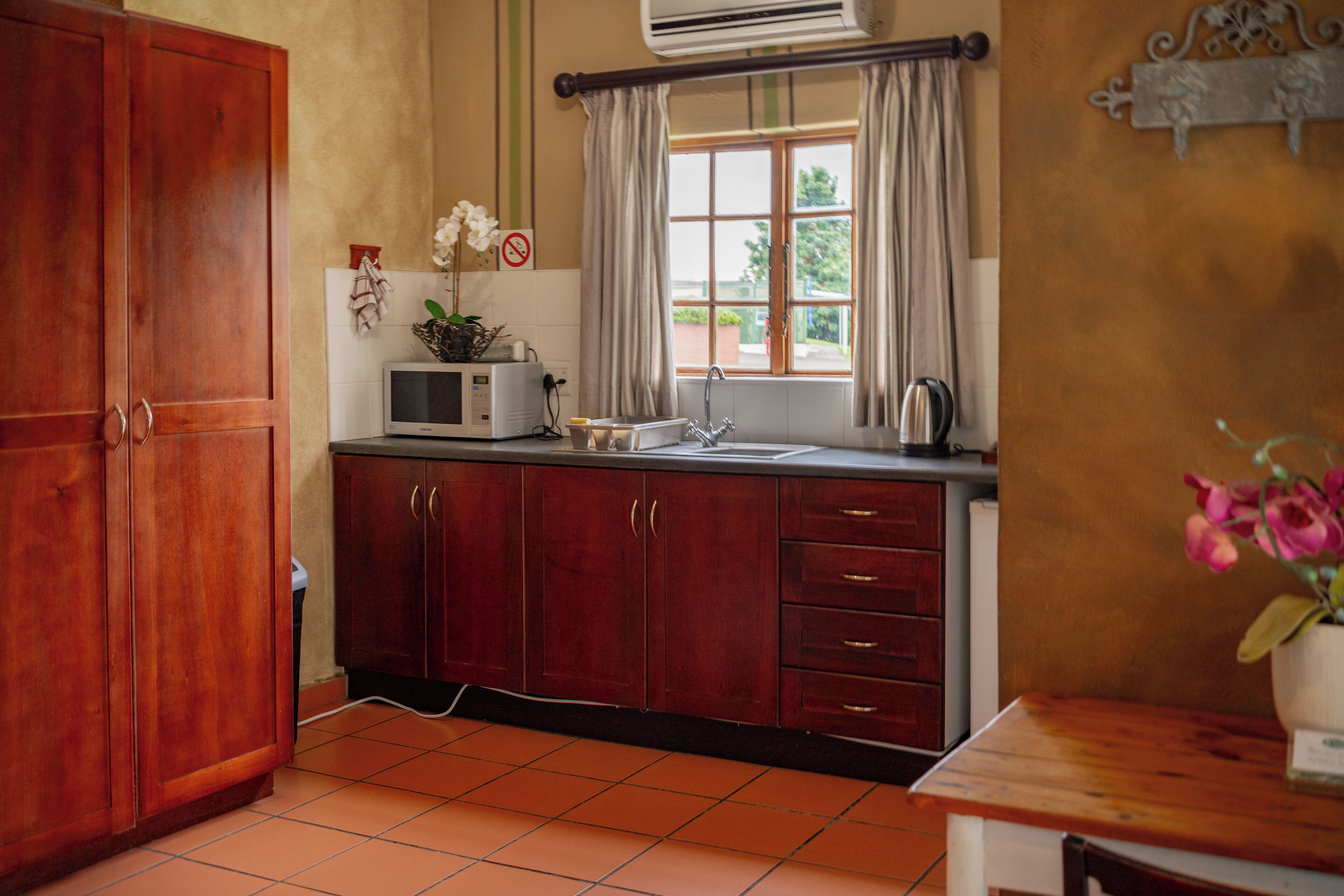 Een keuken met houten kastjes, een magnetron, een spoelbak en een raam met gordijnen.