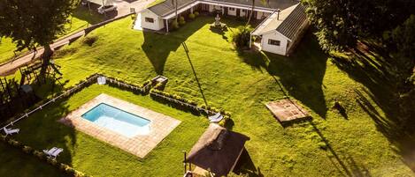 An aerial view of a residential property with a swimming pool, a covered patio, and a well-maintained lawn.