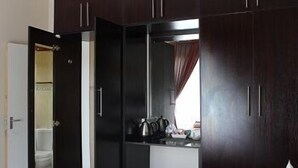 A room with a wardrobe, a small table with a kettle, and a window with curtains.