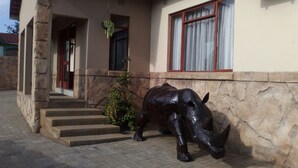 A building with a stone exterior, a set of concrete steps leading to a door, and a large bronze statue of a rhinoceros on the ground.
