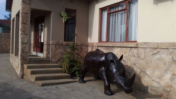Un edificio de fachada de piedra, con una escalera de concreto que lleva a una puerta y una gran estatua de bronce de un rinoceronte en el suelo.